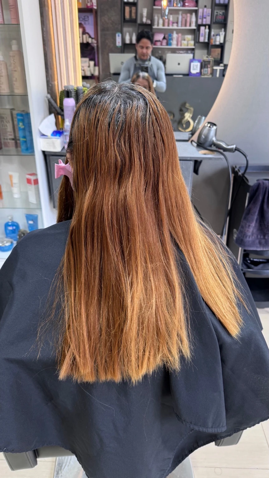 Vista posterior de cabello con raíces oscuras y largos cobrizos en el salón.